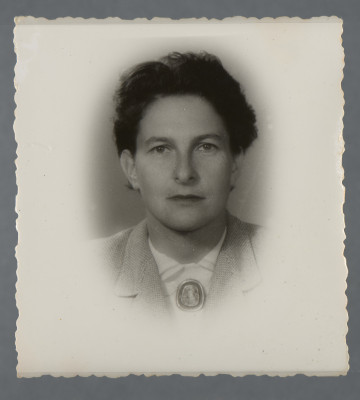 Fotografia portretowa, monochromatyczna, kobiety w wieku być może około czterdziestu lat, ustawionej en face, popiersie. Widoczna biała koszula z broszką przy kołnierzu, jasna marynarka. Ciemne półdługie włosy. Fotografia prostokątna, obraz wywołany w owalu (dookoła biały margines) z rozmytymi krawędziami.Na rewersie widoczne w rogu kółko (?) długopisem, a pośrodku numer ołówkiem, być może roboczy z zakładu fot.: 136