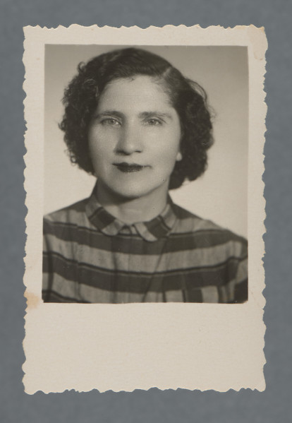 Fotografia monochromatyczna, portretowa kobiety, en face, popiersie; w paskowanej bluzce, z mocno kręcącymi się włosami, ciemnymi. Uśmiecha się. Tło białe. Kadr niesymetryczny (sylwetka wyraźnie po lewej).Krawędzie ząbkowane, wzdłuż nich prostokątny margines, największy przy dolnej krawędzi.