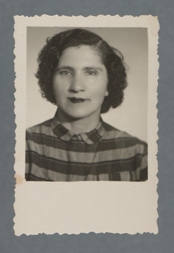 Fotografia monochromatyczna, portretowa kobiety, en face, popiersie; w paskowanej bluzce, z mocno kręcącymi się włosami, ciemnymi. Uśmiecha się. Tło białe. Kadr niesymetryczny (sylwetka wyraźnie po lewej).Krawędzie ząbkowane, wzdłuż nich prostokątny margines, największy przy dolnej krawędzi.