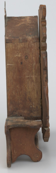 Pięciokątna szafka osadzona na prostokątnej podstawie. W dolnej części podstawy drążek. Drzwiczki do szafki z owalnym lustrem w rzeźbionej ramie o nieregularnym konturze, osadzone na dwóch zawiasach, zamykane na podłużny haczyk. W środku miejsce na schowanie drobnych rzeczy. Z dwóch stron lustra umieszczone są stojące lwy, z głowami odwróconymi na zewnątrz. Nad i pod lustrem rzeźbione motywy floralne i liście. Lwie grzywy oraz tło są w ciemniejszym odcieniu drewna. Na szczycie szafki, z tyłu, umieszczona została blaszana zawieszka. 