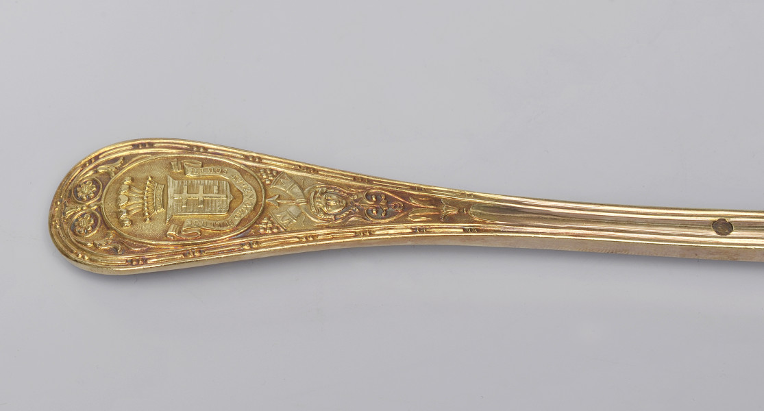 zbliżenie na półkoliście zakończony trzonek z herbem Potockich Pilawa – rewers. Herb pod koroną hrabiowską ze strusimi piórami i napisem obiegającym tarczę od dołu.