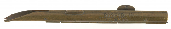 Metalowa, podłużna nabijarka do tytoniu w kolorze złotym, składa się z otwieranej rynienki, na której znajduje się wygrawerowany napis w języku polskim: J. Rosenblum | Leszno 24 |. 