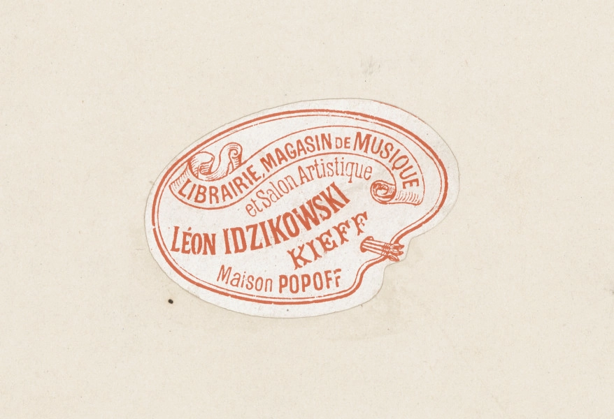 zbliżenie na naklejkę na rewersie karty albumu. Wklejka w kształcie palety malarskiej, na której napis: Librairie, Magasin de Musique et Salon Artistique Léon Idzikowski Kieff Maison Popoff