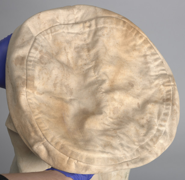 Pokrowiec jest w kolorze jasnobrązowym z napisami koloru zielonego w języku angielskim:  107/III ; CD[?]T.G[?]FF. BUSSGANG ; 10A ST. JOHN CAMP ; SERVICEMEN STUDENTS' CENTRE ; HIGH WYCOMBE ; WENX[?] W6[?]5394. W górnej części, po lewej stronie znajdują się skórzane rzemyki służące do wiązania całości pokrowca. W wewnętrznej części pokrowca widoczny fragment naszywki (prawdopodobnie metki) w kolorze jasnobrązowym.