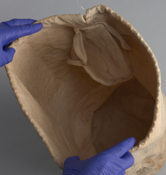 Pokrowiec jest w kolorze jasnobrązowym z napisami koloru zielonego w języku angielskim:  107/III ; CD[?]T.G[?]FF. BUSSGANG ; 10A ST. JOHN CAMP ; SERVICEMEN STUDENTS' CENTRE ; HIGH WYCOMBE ; WENX[?] W6[?]5394. W górnej części, po lewej stronie znajdują się skórzane rzemyki służące do wiązania całości pokrowca. W wewnętrznej części pokrowca widoczny fragment naszywki (prawdopodobnie metki) w kolorze jasnobrązowym.