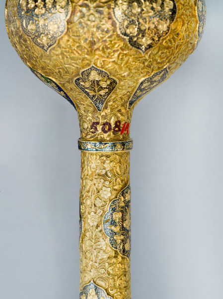 zbliżenie na numer inwentarzowy. Nad niellowanym pierścieniem umieszczonym na rękojeści, pod kulistą gałką czerwono-brązowy numer inwentarzowy.