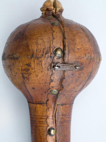 zbliżenie na głowicę futerału zapinaną na skobelek z haczykiem. Wzdłuż krawędzi ząbkowana skóra i metalowe guzy.