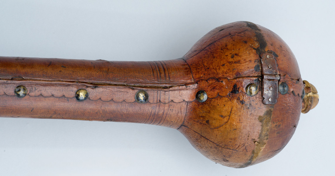 zbliżenie na głowicę futerału - ujęcie z boku. Wzdłuż krawędzi etui skóra ząbkowana, z metalowymi guzami i zawiasem na głowicy.