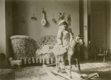 Jerzy Rafał Lubomirski jako dziecko siedzi na koniu na biegunach. Lubomirski ma długie włosy, a z tyłu na  scianie wiszą instrumenty muzyczne.