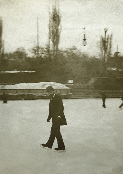 Na zdjeciu znajduje się mężczyzna w meloniku jadący na łyżwach.