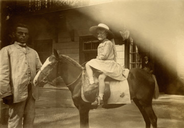Fotografia przedstawia kilkuletnią dziewczynkę siedzącą w damskim siodle na kucu, obok niej stoi pracownik ordynacji przeworskiej. 