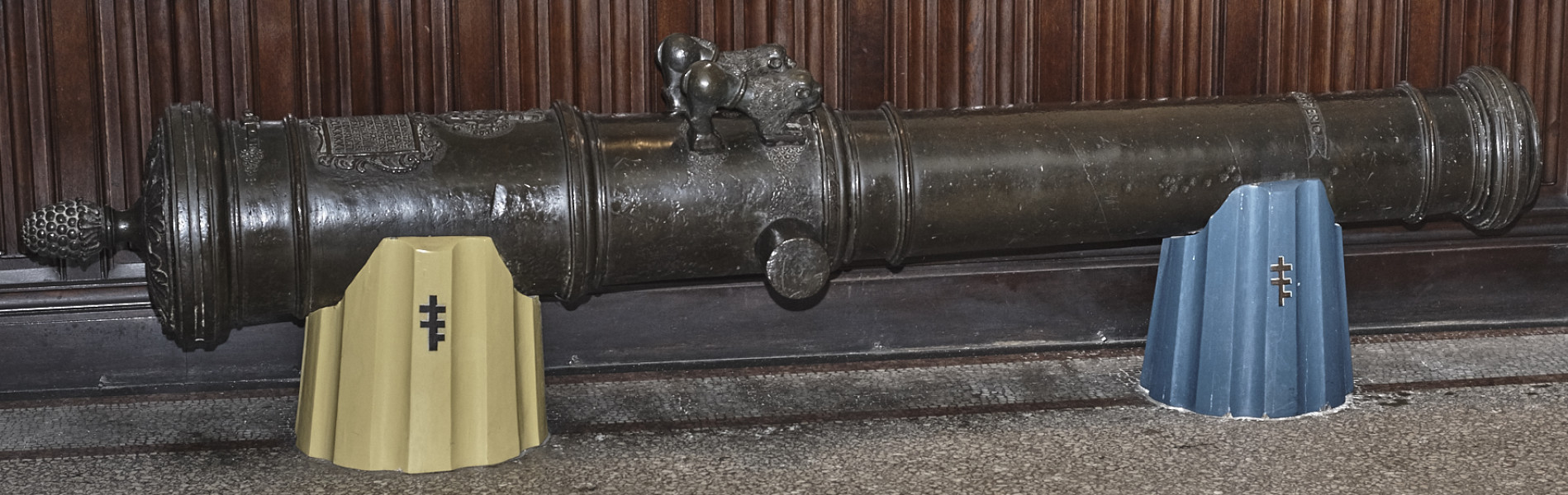 Na zdjęciu znajduje się lufa armatnia wsparta na dwóch drewnianych postumentach ozdobionych herbem Pilawa.