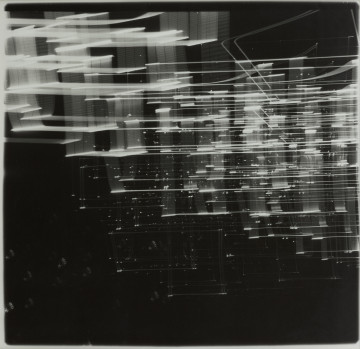 fotografia - Ujęcie z przodu. Czarno-biała fotografia abstrakcyjna zakomponowana poziomo. Jasne, nieregularne i nieostre horyzontalne struktury, zintensyfikowane w lewej górnej częsci pracy, rozświetlają czarne tło. Tworzą dynamiczną siatkę punktów i rozmytych płaszczyzn światła, które zmniejszają się i zanikają schodząc łagodnie w dół ku prawej krawędzi pracy.