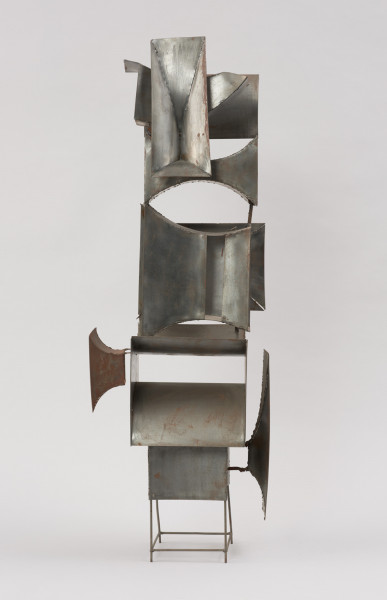 rzeźba; instalacja; Okna V - ujęcie z lewej strony. Ażurowa konstrukcja przestrzenna z geometrycznych, blaszanych elementów przyspawanych do drucianego stelażu. Do metalowych prętów, z czterech stron, na różnych wysokościach, pionowo bądź poziomo przyspawano elementy przypominające prostokątne głośniki tubowe (bryły niewypukłe o ścianach w kształcie podwójnie hiperbolicznym, półwalcowatym, trójkątnym lub czworokątnym z brakującą jedną lub dwoma ścianami). U dołu widoczny stelaż, tworzący krótkie, cienkie, pionowe nóżki poprzecznie ze sobą połączone.