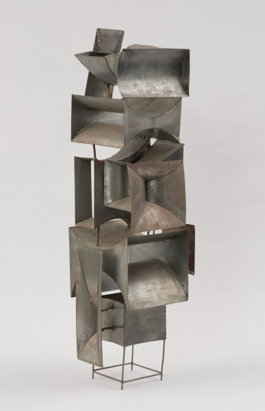 rzeźba; instalacja; Okna V - ujęcie z tyłu skosem w prawą stronę. Ażurowa konstrukcja przestrzenna z geometrycznych, blaszanych elementów przyspawanych do drucianego stelażu. Do metalowych prętów, z czterech stron, na różnych wysokościach, pionowo bądź poziomo przyspawano elementy przypominające prostokątne głośniki tubowe (bryły niewypukłe o ścianach w kształcie podwójnie hiperbolicznym, półwalcowatym, trójkątnym lub czworokątnym z brakującą jedną lub dwoma ścianami). U dołu widoczny stelaż, tworzący krótkie, cienkie, pionowe nóżki poprzecznie ze sobą połączone.