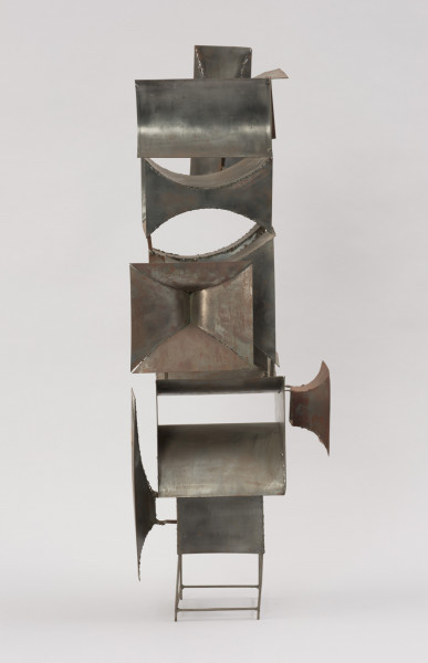 rzeźba; instalacja; Okna V - ujęcie prawego boku. Ażurowa konstrukcja przestrzenna z geometrycznych, blaszanych elementów przyspawanych do drucianego stelażu. Do metalowych prętów, z czterech stron, na różnych wysokościach, pionowo bądź poziomo przyspawano elementy przypominające prostokątne głośniki tubowe (bryły niewypukłe o ścianach w kształcie podwójnie hiperbolicznym, półwalcowatym, trójkątnym lub czworokątnym z brakującą jedną lub dwoma ścianami). U dołu widoczny stelaż, tworzący krótkie, cienkie, pionowe nóżki poprzecznie ze sobą połączone.