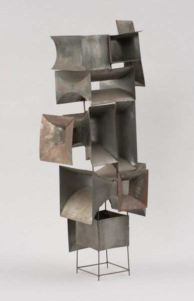 rzeźba; instalacja; Okna V - ujęcie z przodu skosem w prawą stronę.  Ażurowa konstrukcja przestrzenna z geometrycznych, blaszanych elementów przyspawanych do drucianego stelażu. Do metalowych prętów, z czterech stron, na różnych wysokościach, pionowo bądź poziomo przyspawano elementy przypominające prostokątne głośniki tubowe (bryły niewypukłe o ścianach w kształcie podwójnie hiperbolicznym, półwalcowatym, trójkątnym lub czworokątnym z brakującą jedną lub dwoma ścianami). U dołu widoczny stelaż, tworzący krótkie, cienkie, pionowe nóżki poprzecznie ze sobą połączone.