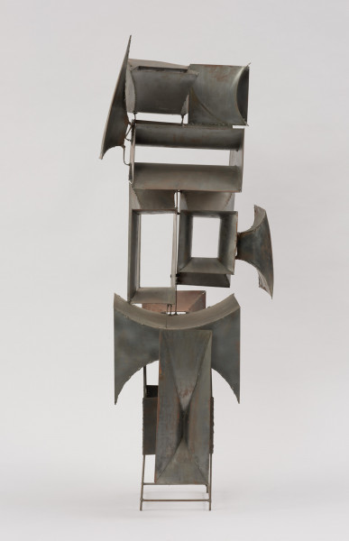 rzeźba; instalacja; Okna V - ujęcie z tyłu. Ażurowa konstrukcja przestrzenna z geometrycznych, blaszanych elementów przyspawanych do drucianego stelażu. Do metalowych prętów, z czterech stron, na różnych wysokościach, pionowo bądź poziomo przyspawano elementy przypominające prostokątne głośniki tubowe (bryły niewypukłe o ścianach w kształcie podwójnie hiperbolicznym, półwalcowatym, trójkątnym lub czworokątnym z brakującą jedną lub dwoma ścianami). U dołu widoczny stelaż, tworzący krótkie, cienkie, pionowe nóżki poprzecznie ze sobą połączone.