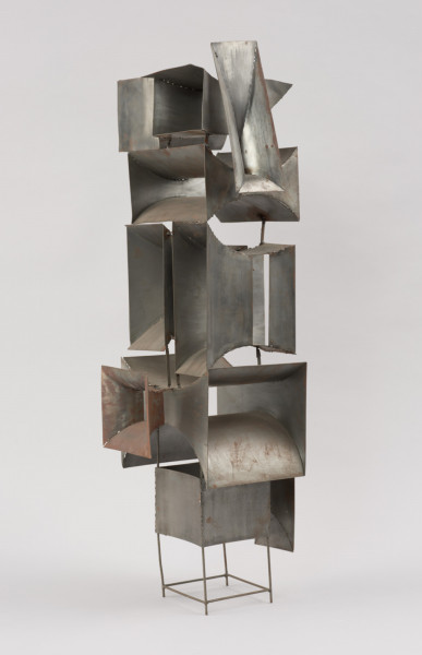 rzeźba; instalacja; Okna V - ujęcie z przodu skosem w lewą stronę.  Ażurowa konstrukcja przestrzenna z geometrycznych, blaszanych elementów przyspawanych do drucianego stelażu. Do metalowych prętów, z czterech stron, na różnych wysokościach, pionowo bądź poziomo przyspawano elementy przypominające prostokątne głośniki tubowe (bryły niewypukłe o ścianach w kształcie podwójnie hiperbolicznym, półwalcowatym, trójkątnym lub czworokątnym z brakującą jedną lub dwoma ścianami). U dołu widoczny stelaż, tworzący krótkie, cienkie, pionowe nóżki poprzecznie ze sobą połączone.