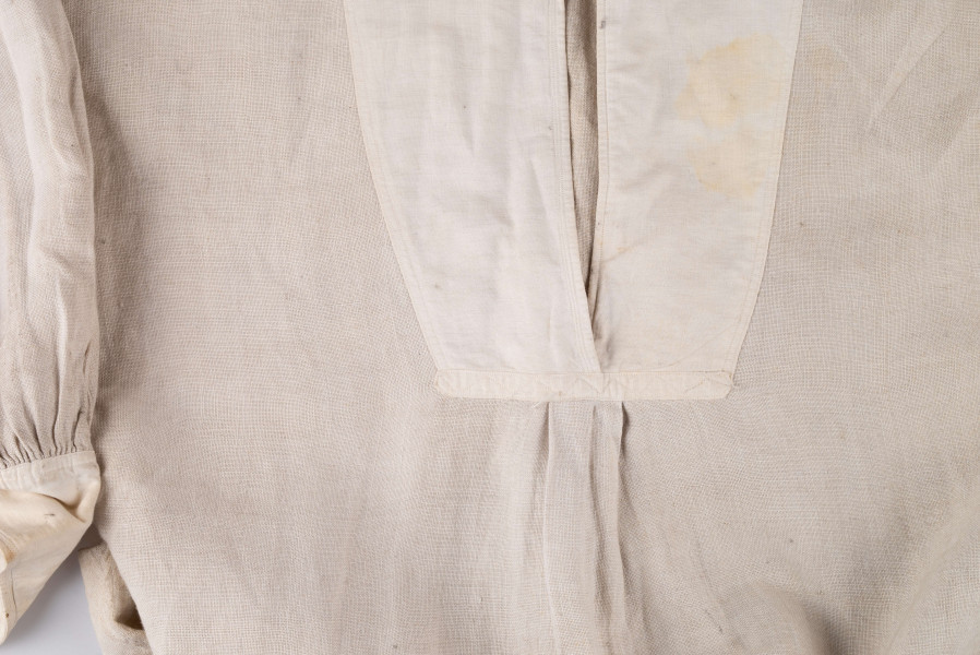 E/128/MRK/ML - Koszula lniana męska, biała, prosty i krótki kołnierzyk zapinany na 2 guziki, rękawy długie zapinane na 2 guziki. Dł. 101 cm, szer. 54 cm. Dł. rękawa 57 cm, szer. 20 cm, dł. mankietu 5 cm, szer. 11 cm. Z przodu koszuli rozcięcie  dł. 37 cm.  