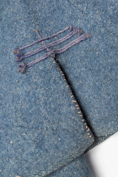 E/308/MRK/ML - Sukmana męska szaro-granatowa z metalowymi guzikami. Kołnierz - stójka dł. 43 cm, szer. 5 cm, rękaw wszywany prosty dł. 56 cm, szer. 15 cm. Krój prosty, w pasie po obu stronach zaszewki /13/, lniana podszewka, sukmana zapina na 6 haftek, ozdobiona taśmą szer. 1 cm i metalowymi guzami /7/. Dł. 123 cm, szer. 49 cm.