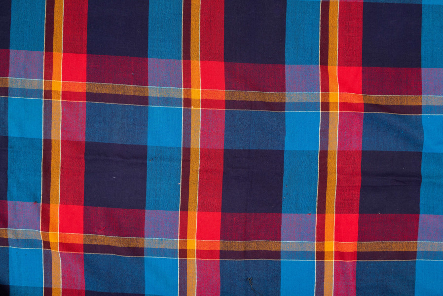 E/126/MRK/ML - Chustka kratówka wełniana. W kolorach: niebieski, czerwony, brązowy i czarny. Na brzegach kolorowe frędzle. Długość frędzli 14 cm. Wymiary chusty 160 x 150 cm. Wymiary krat: większe 12,5 x 11,5, najmiejsza 2 x 1,5 cm. Chusta częściowo podziurawiona. 