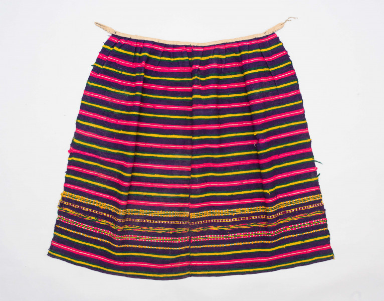 E/125/MRK/ML - Zapaska wełniana w różnokolorowe pasy, ułożone poziomo. Dł. zapaski 77 cm, szer. 98 cm, zszyta w środku. Kolory: fioletowy, niebieski, czerwony, biały, zielony, żółty, brązowy. Od góry 14 zakładek na nich naszyty lniany pasek szer. 1 cm, dł. 65 cm.