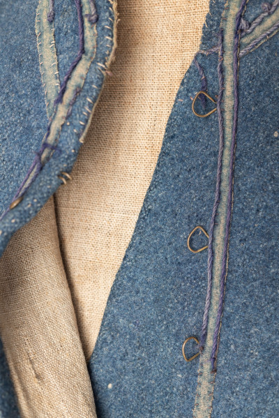 E/308/MRK/ML - Sukmana męska szaro-granatowa z metalowymi guzikami. Kołnierz - stójka dł. 43 cm, szer. 5 cm, rękaw wszywany prosty dł. 56 cm, szer. 15 cm. Krój prosty, w pasie po obu stronach zaszewki /13/, lniana podszewka, sukmana zapina na 6 haftek, ozdobiona taśmą szer. 1 cm i metalowymi guzami /7/. Dł. 123 cm, szer. 49 cm.