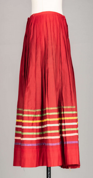 E/516/MRK/ML - Spódnica krakowska. Wykonana z wełenki, kolor czerwony. W dolnej czesci spódnica ozdobiona różnokolorowymi tasiemkami, sztuk 7. Przy oszewce lekko marszczona.