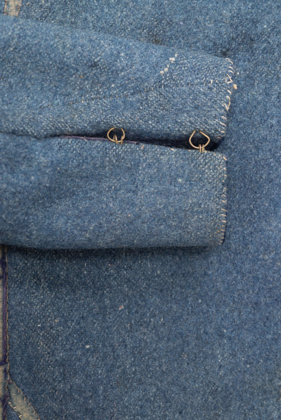 E/308/MRK/ML - Sukmana męska szaro-granatowa z metalowymi guzikami. Kołnierz - stójka dł. 43 cm, szer. 5 cm, rękaw wszywany prosty dł. 56 cm, szer. 15 cm. Krój prosty, w pasie po obu stronach zaszewki /13/, lniana podszewka, sukmana zapina na 6 haftek, ozdobiona taśmą szer. 1 cm i metalowymi guzami /7/. Dł. 123 cm, szer. 49 cm.