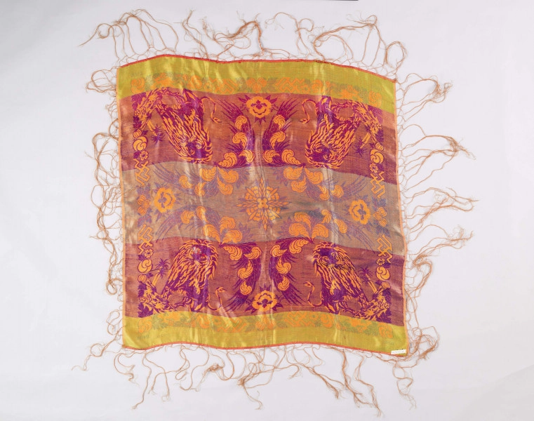 E/127/MRK/ML - Chustka jedwabna różnokolorowa z frędzlami dług. 30 cm. Długość chustki 105 cm, szerokość 100 cm. Kolory: czerwony, zielony, żółty, fioletowy, niebieski. Frędzle koloru czerwonego. Chusta zdobiona motywami kwiatowymi, a w każdym rogu wizerunek tygrysa. 