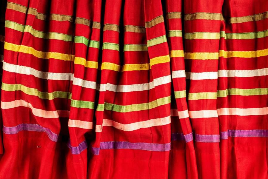 E/516/MRK/ML - Spódnica krakowska. Wykonana z wełenki, kolor czerwony. W dolnej czesci spódnica ozdobiona różnokolorowymi tasiemkami, sztuk 7. Przy oszewce lekko marszczona.