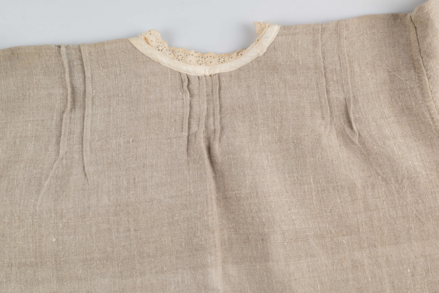 E/529/MRK/ML - Koszula damska. Uszyta z lnianego płótna z długimi rękawami, pod szyją dziurkowa pliska w kolorze białym. Na linii ramienia symetryczne zaszewki, pod szyjką pęknięcie zapinane na guzik.