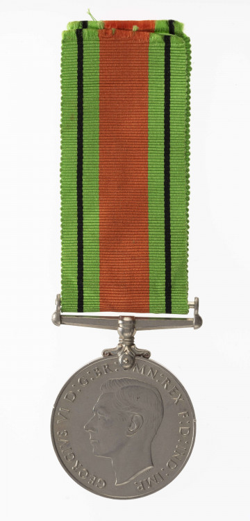 H/2050/MRK/ML - Odznaką jest medal bity w miedzioniklu 3,6 cm średnicy, o gładkim rancie. Na awersie jest lewy profil głowy króla Jerzego VI, przy zarycie szyi sygnatura HP. W otoku napis: GREGORIUS VI D:G:BR:OMN:REX F:D:IND:IMP. Na rewersie dąb zwięczony koroną zamkniętą, oraz dwa ryczące, wspięte na tylnych łapach lwy, za ich grzbietami daty 1939 i 1945. Dąb wyrasta z lądu oblanego wodą (wyspa). Poniżej w dwóch wierszach napis: THE DEFENCE MEDAL. Przywieszka w formie szlufy na wstążkę nitowana z medalem. Wstążka szerokości 3,2 cm, od brzegów jasnozielone pasy z czarnym prążkiem, w środku pas pomarańczowo-ceglasty.