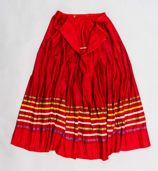 E/516/MRK/ML - Spódnica krakowska. Wykonana z wełenki, kolor czerwony. W dolnej czesci spódnica ozdobiona różnokolorowymi tasiemkami, sztuk 7. Przy oszewce lekko marszczona.