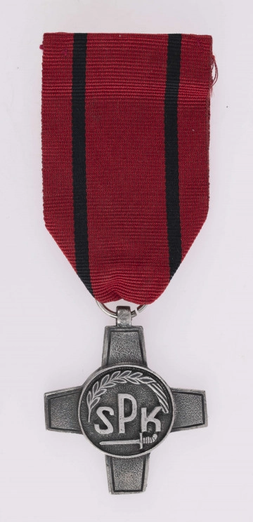H/2463/MRK/ML - Odznaką jest krzyż bity w białym metaluo obramowanych ramionach, w środku okrągła tarcza z napisem SPK poniżej miecz, u góry otokowo kłos, wstążka czerwona z 2 czarnymi paskami.
