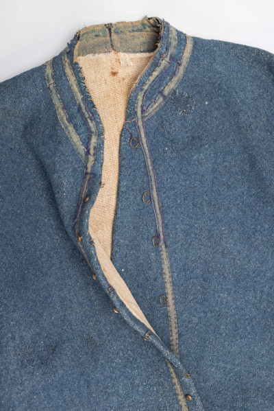 E/308/MRK/ML - Sukmana męska szaro-granatowa z metalowymi guzikami. Kołnierz - stójka dł. 43 cm, szer. 5 cm, rękaw wszywany prosty dł. 56 cm, szer. 15 cm. Krój prosty, w pasie po obu stronach zaszewki /13/, lniana podszewka, sukmana zapina na 6 haftek, ozdobiona taśmą szer. 1 cm i metalowymi guzami /7/. Dł. 123 cm, szer. 49 cm.