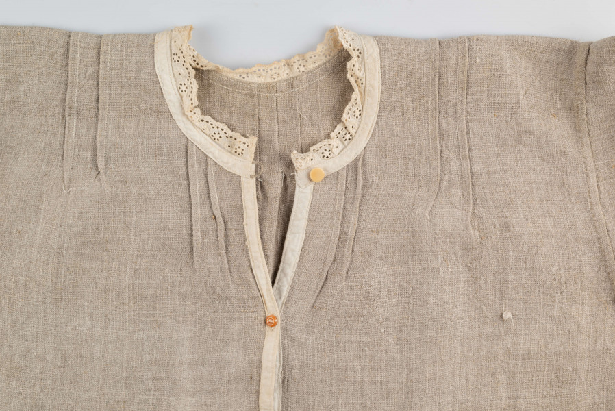 E/529/MRK/ML - Koszula damska. Uszyta z lnianego płótna z długimi rękawami, pod szyją dziurkowa pliska w kolorze białym. Na linii ramienia symetryczne zaszewki, pod szyjką pęknięcie zapinane na guzik.