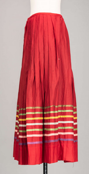 E/516/MRK/ML - Spódnica krakowska. Wykonana z wełenki, kolor czerwony. W dolnej czesci spódnica ozdobiona różnokolorowymi tasiemkami, sztuk 7. Przy oszewce lekko marszczona.