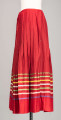 E/516/MRK/ML - Spódnica krakowska. Wykonana z wełenki, kolor czerwony. W dolnej czesci spódnica ozdobiona różnokolorowymi tasiemkami, sztuk 7. Przy oszewce lekko marszczona.