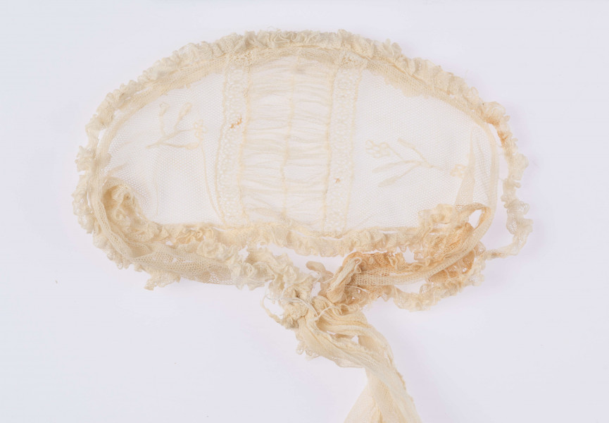 E/124/MRK/ML - Czepek tiulowy, biały tiul, wzory o motywach roślinnych, brzegi pofałdowane. Dług. wstążek 45 cm, szer. 8 cm, brzegi obszyte białą koronką szer. 1 cm. Czepek dł. 50 cm szer. 18 cm. W części środkowej wstawka szer. 10 cm.