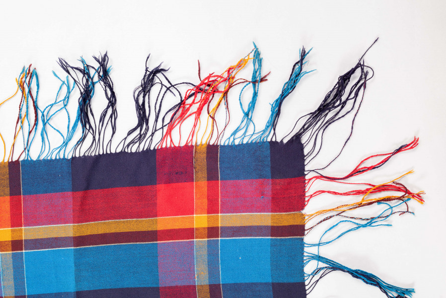 E/126/MRK/ML - Chustka kratówka wełniana. W kolorach: niebieski, czerwony, brązowy i czarny. Na brzegach kolorowe frędzle. Długość frędzli 14 cm. Wymiary chusty 160 x 150 cm. Wymiary krat: większe 12,5 x 11,5, najmiejsza 2 x 1,5 cm. Chusta częściowo podziurawiona. 