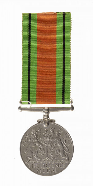 Odznaką jest medal bity w miedzioniklu średnicy 3,6cm, o gładkim rancie. Na awersie lewy profil głowy króla Jerzego VI. Przy zarysie szyi sygnatura HP. W otoku napis: Gregorius VI D:G:BR:OMN:REX F:D:IND:IMP. Na rewersie dąb wyrastający z lądu oblanego wodą, nad nim korona zamknięta. Po bokach dwa ryczące lwy, wspięte na tylnych łapach, przy rancie daty 1939  i 1945. U dułu w 2 wierszach napis: THE DEFENCE MEDAL. Przywieszka  w formie szlufy  na wstążkę nitowana do medalu. Wstążka szerokości 3,2 cm, od brzegów zielone pasy z czarnymi prążkimi wśrodku pas pomarańczowo-ceglasty