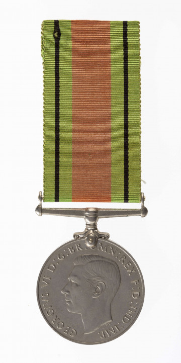 Odznaką jest medal bity w miedzioniklu średnicy 3,6cm, o gładkim rancie. Na awersie lewy profil głowy króla Jerzego VI. Przy zarysie szyi sygnatura HP. W otoku napis: Gregorius VI D:G:BR:OMN:REX F:D:IND:IMP. Na rewersie dąb wyrastający z lądu oblanego wodą, nad nim korona zamknięta. Po bokach dwa ryczące lwy, wspięte na tylnych łapach, przy rancie daty 1939  i 1945. U dułu w 2 wierszach napis: THE DEFENCE MEDAL. Przywieszka  w formie szlufy  na wstążkę nitowana do medalu. Wstążka szerokości 3,2 cm, od brzegów zielone pasy z czarnymi prążkimi wśrodku pas pomarańczowo-ceglasty