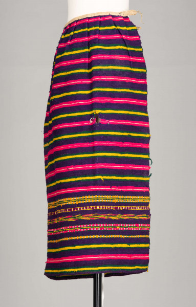 E/125/MRK/ML - Zapaska wełniana w różnokolorowe pasy, ułożone poziomo. Dł. zapaski 77 cm, szer. 98 cm, zszyta w środku. Kolory: fioletowy, niebieski, czerwony, biały, zielony, żółty, brązowy. Od góry 14 zakładek na nich naszyty lniany pasek szer. 1 cm, dł. 65 cm.