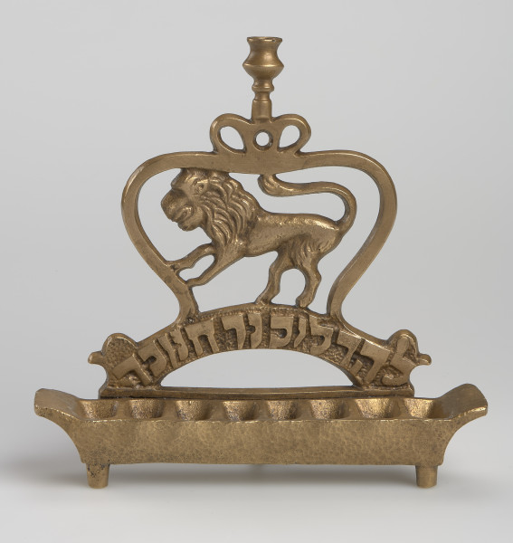 Świecznik chanukowy (hebr. chanukija) - Lampka o podstawie na trzech nóżkach, z wywiniętymi do góry krawędziami bocznymi. Osiem wgłębień. Podstawę zaplecka tworzy łuk - z napisem - sięgający skrajnych wgłębień. Górna część zaplecka naśladuje kontur zamkniętej korony, wewnątrz której znajduje się lew, zwrócony w lewo, oparty tylnymi łapami o łuk, a przednimi o koronę, ogon ma esowato wywinięty, sięgający centralnej, górnej części korony.