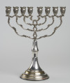 Świecznik chanukowy (hebr. chanukija) - Świecznik na okrągłej, stopniowanej podstawie. Trzonek prosty z tralką, do niego mocowane śrubą cztery pary ramion wychodzące z wspólnego trzonka, z delikatnym ornamentem kwiatowo-wolutowym. Osiem tulejek w kształcie amfor, połączone po cztery poziomym ornamentowym wspornikiem.