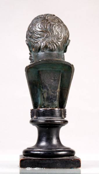 Zdjęcie przedstawia tylną część popiersia mężczyzny, z głową pochyloną w dół. Twarz ma pociągłą, z długim nosem, ze zmarszczkami, okoloną brodą. Włosy ułożone w kręte kosmyki zachodzące na czoło i skronie.