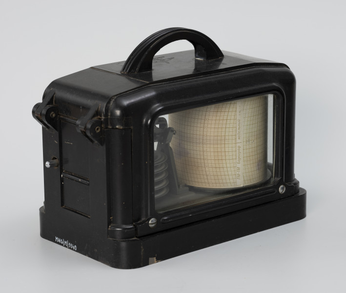 Barograf okrętowy - ujęcie ze skosu z lewej; Barometr w czarnej, ebonitowej obudowie, oszklonej z trzech stron. Szyby wsunięte w osłonę i zablokowane od spodu płaskownikami, na 2 wkręty. Osłona przymocowana do obudowy dwoma zawiasami, zamykana na zamek zatrzaskowy. Na górnej powierzchni osłony łukowaty uchwyt do zawieszenia na haku w kabinie. W środku obudowy na metalowej podstawie, znajduje się system 5 puszek Vidiego oraz system dźwigni (przekładni). Na bębnie znajduje się pas papieru, barogram z nadrukiem skali czasowej (fragmenty łuku w cyklu 24godz./na dzień -linia co 2 godz.) i ciśnienia (linie poziome co 10 hPa). Barogram jest wyskalowany w zakresie od 950 do 1050 hPa. W miejscu sklejenia pasa barogramu napis ŁM-1M Barograf/ Niebielnyj. W tylnej części obudowy pod zawiasami dźwignia unieruchamiająca i odsuwająca pisak od paska barogramu.