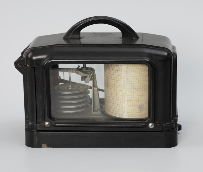 Barograf okrętowy - ujęcie z tyłu; Barometr w czarnej, ebonitowej obudowie, oszklonej. Szyby wsunięte w osłonę i zablokowane od spodu płaskownikami, na 2 wkręty. Osłona przymocowana do obudowy dwoma zawiasami, zamykana na zamek zatrzaskowy. Na górnej powierzchni osłony łukowaty uchwyt do zawieszenia na haku w kabinie. W środku obudowy na metalowej podstawie znajduje się system 5 puszek Vidiego oraz system dźwigni (przekładni) przenoszących deformację elementu pomiarowego na wskazówkę zakończoną pisakiem. Na bębnie znajduje się pas papieru, barogram z nadrukiem skali czasowej (fragmenty łuku w cyklu 24godz./na dzień -linia co 2 godz.) i ciśnienia (linie poziome co 10 hPa). Barogram jest wyskalowany w zakresie od 950 do 1050 hPa. W miejscu sklejenia pasa barogramu napis ŁM-1M Barograf/ Niebielnyj. Na obwodzie pasa na górnej krawędzi napisy Poniedielnik, Wtornik, Srieda, Czietwierg, Piatnica, Sybotta, Wozkrasienie.